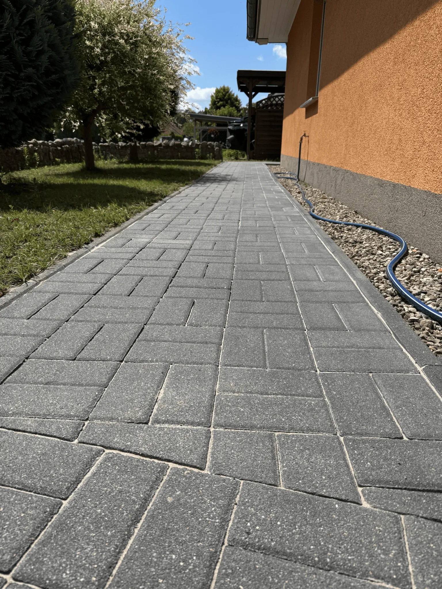 Sauber gereinigte anthrazitfarbene Pflastersteine im Gartenweg neben Hauswand