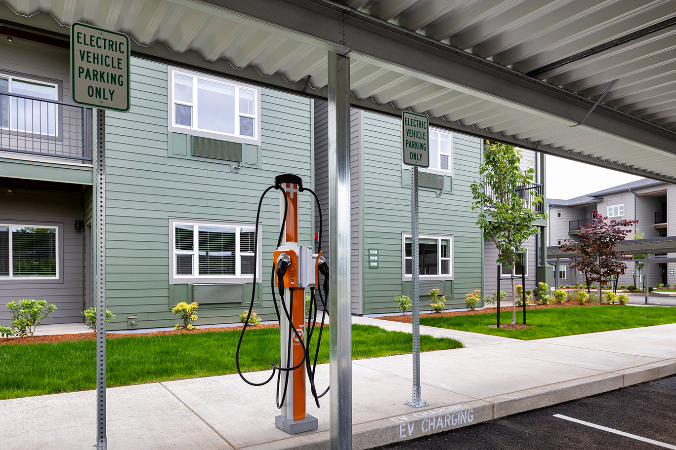 Electric vehicle charging station under a covered parking area adjacent to apartment buildings.