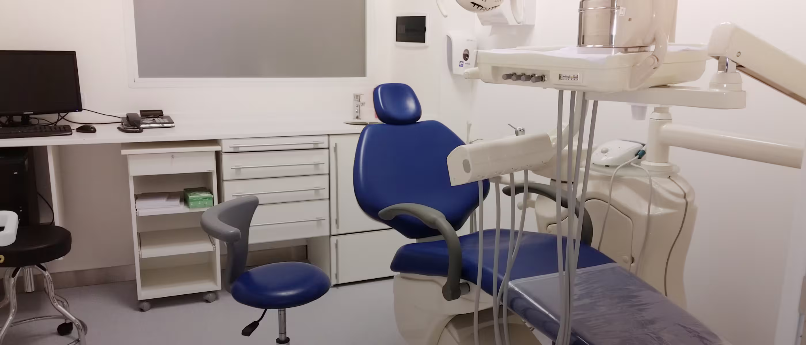 
Consultorio dental con silla azul, computadora y gabinetes blancos
