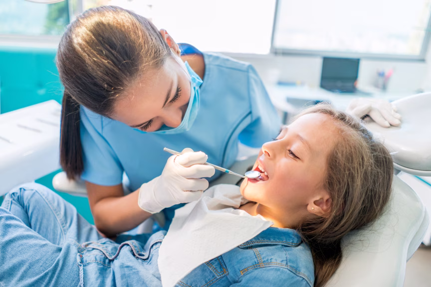 Dentista examinando los dientes de una niña con espejo dental en la consulta