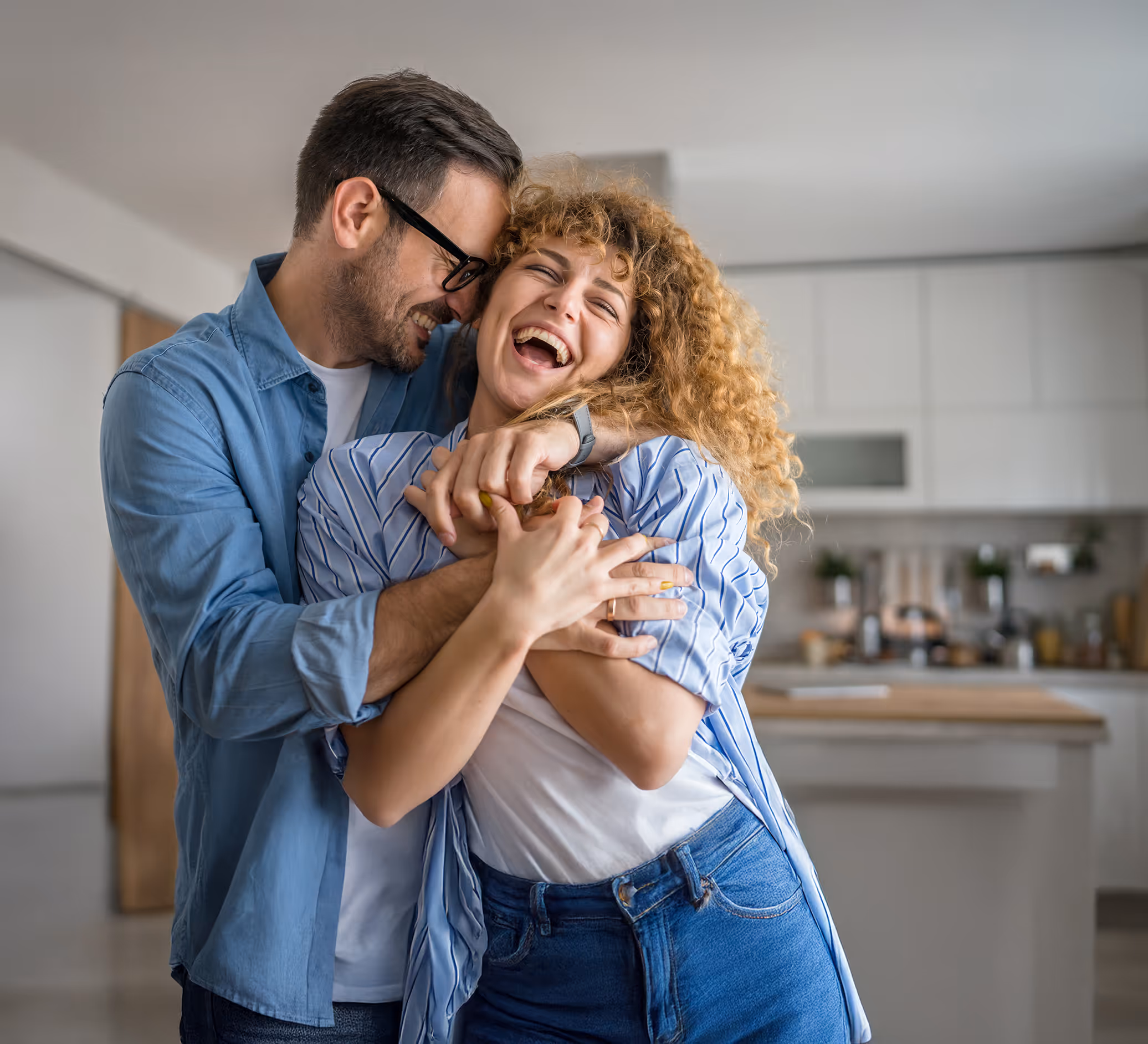 Pareja joven abrazándose y riendo felizmente en una cocina moderna.
