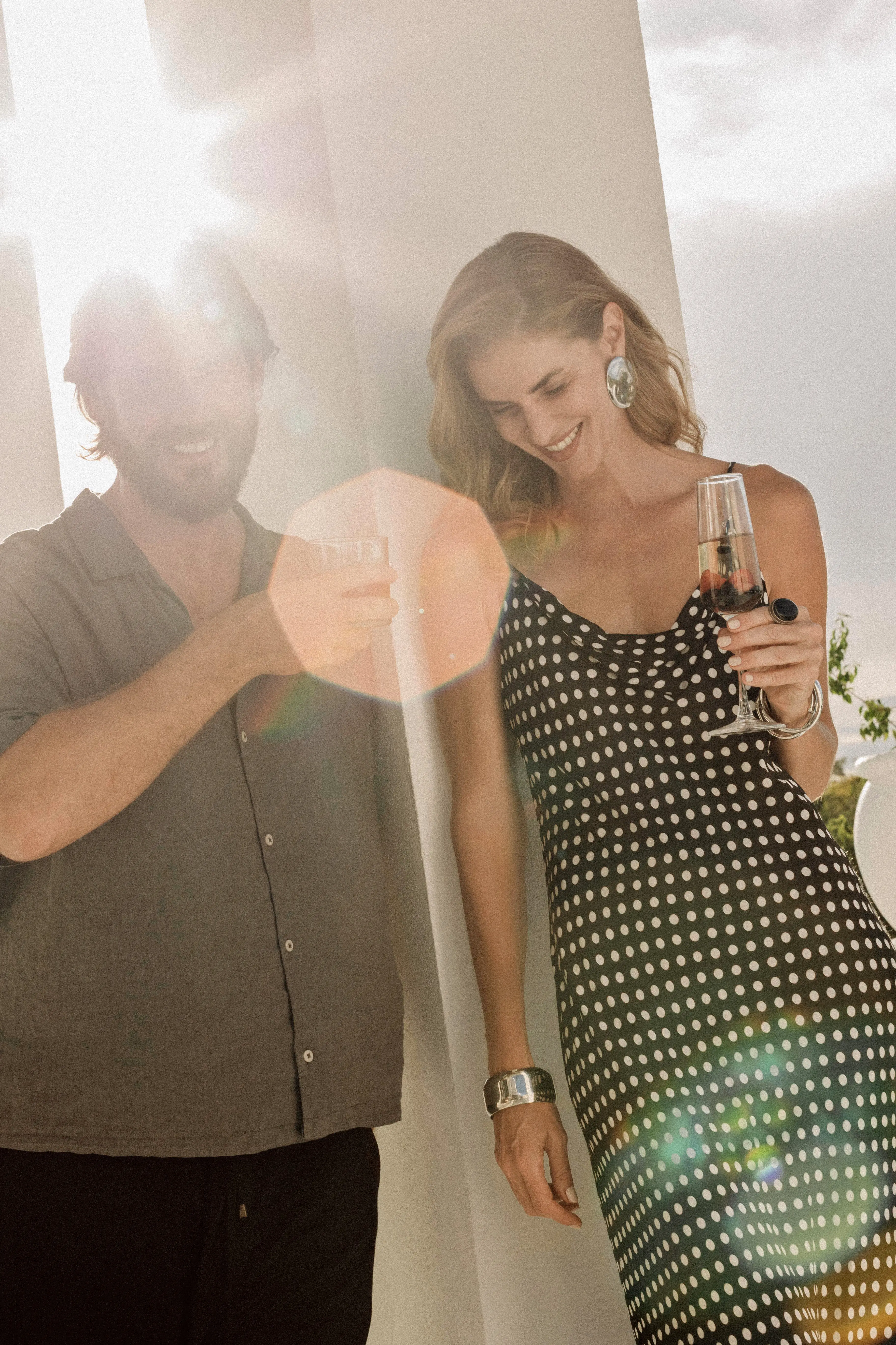 Smiling man and woman enjoying drinks together outdoors with sunlight flare.