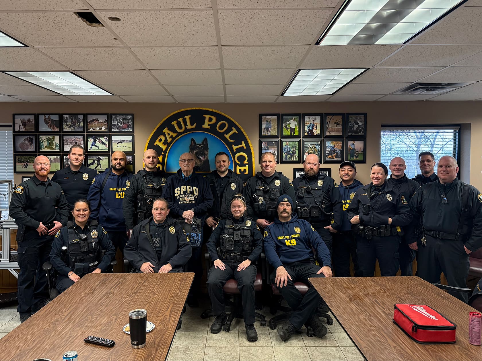 Group of St. Paul Police Department officers and staff posing together in a room with a large St. Paul Police emblem on the wall behind them.