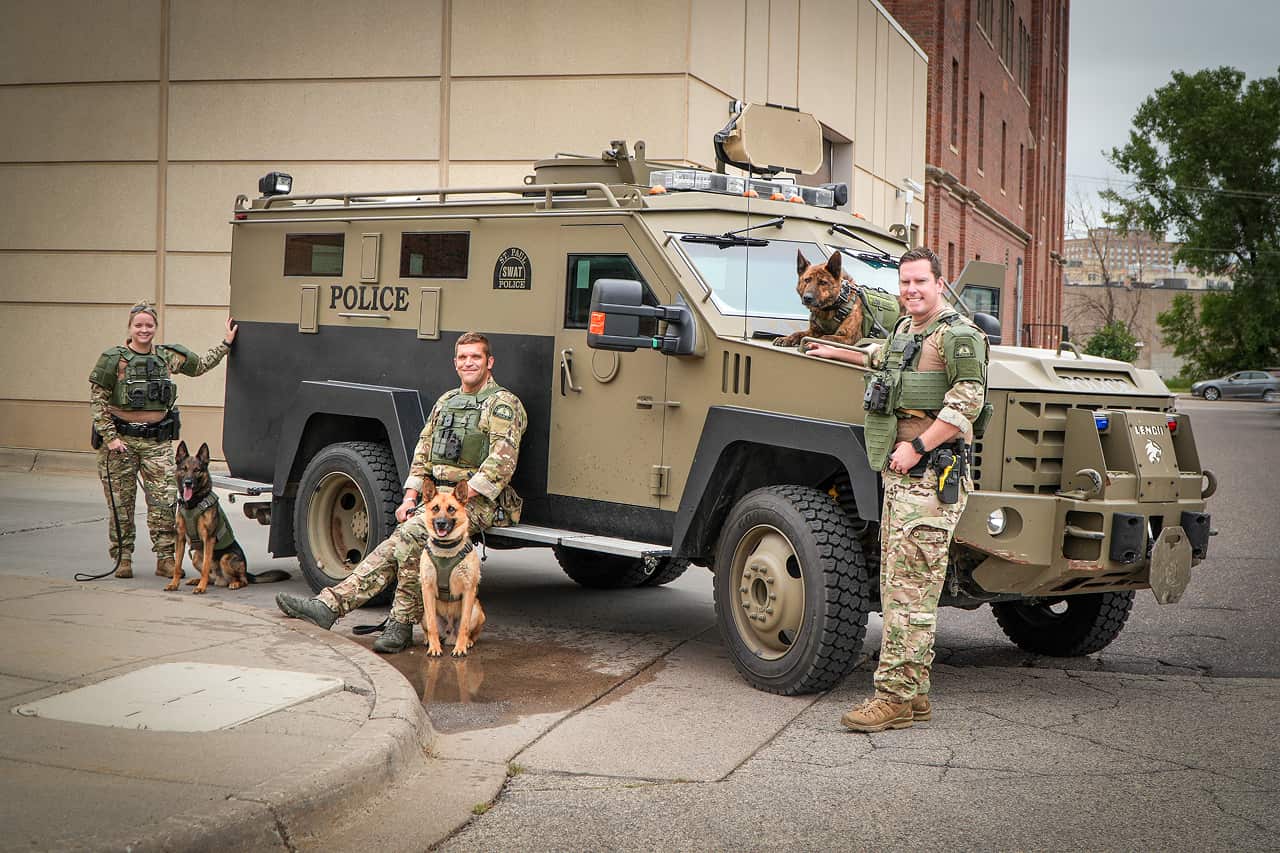 Police K9 unit car parked in snow with a German Shepherd dog walking toward the camera.