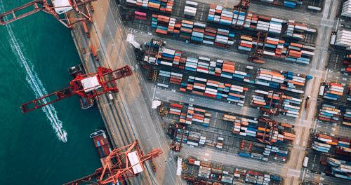 Aerial view of a busy container port with cranes, shipping containers, and cargo ships along the waterfront