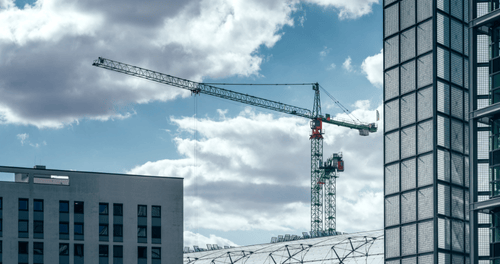 Construction crane positioned between modern buildings against a cloudy blue sky