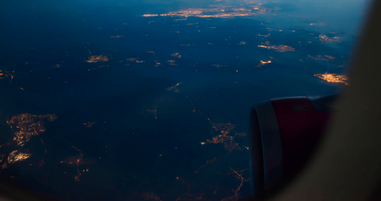 aerial view from an airplane window showing illuminated cities and coastlines at dusk, symbolising aviation networks, global connectivity, and international transport systems. Industries
