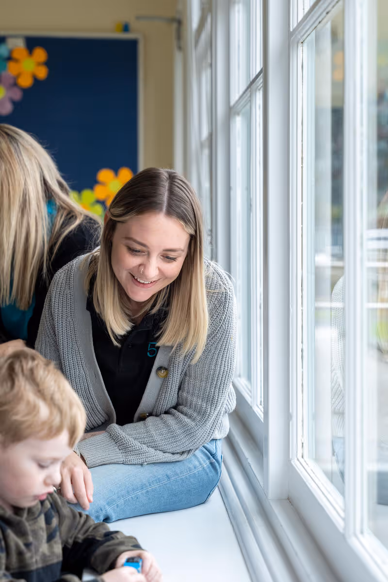 A woman smiling at a young child while reading or looking at something together indoors.