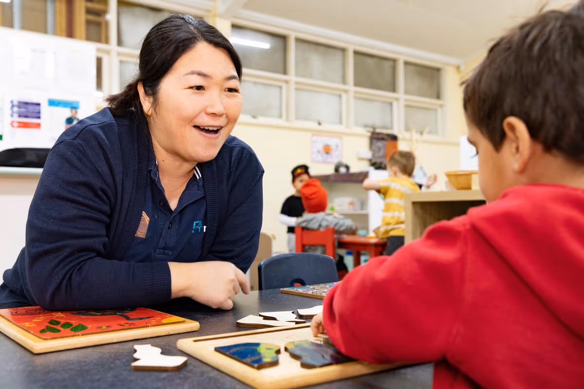A woman sitting with a young child at a table, talking and working together.