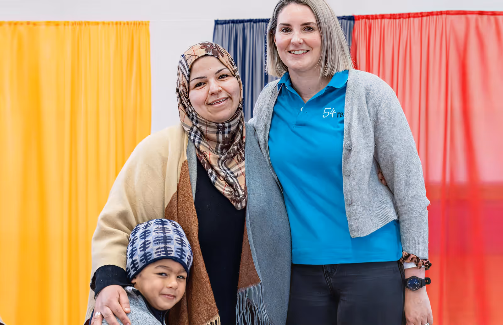 Two women and a young child smiling together at a community event booth.