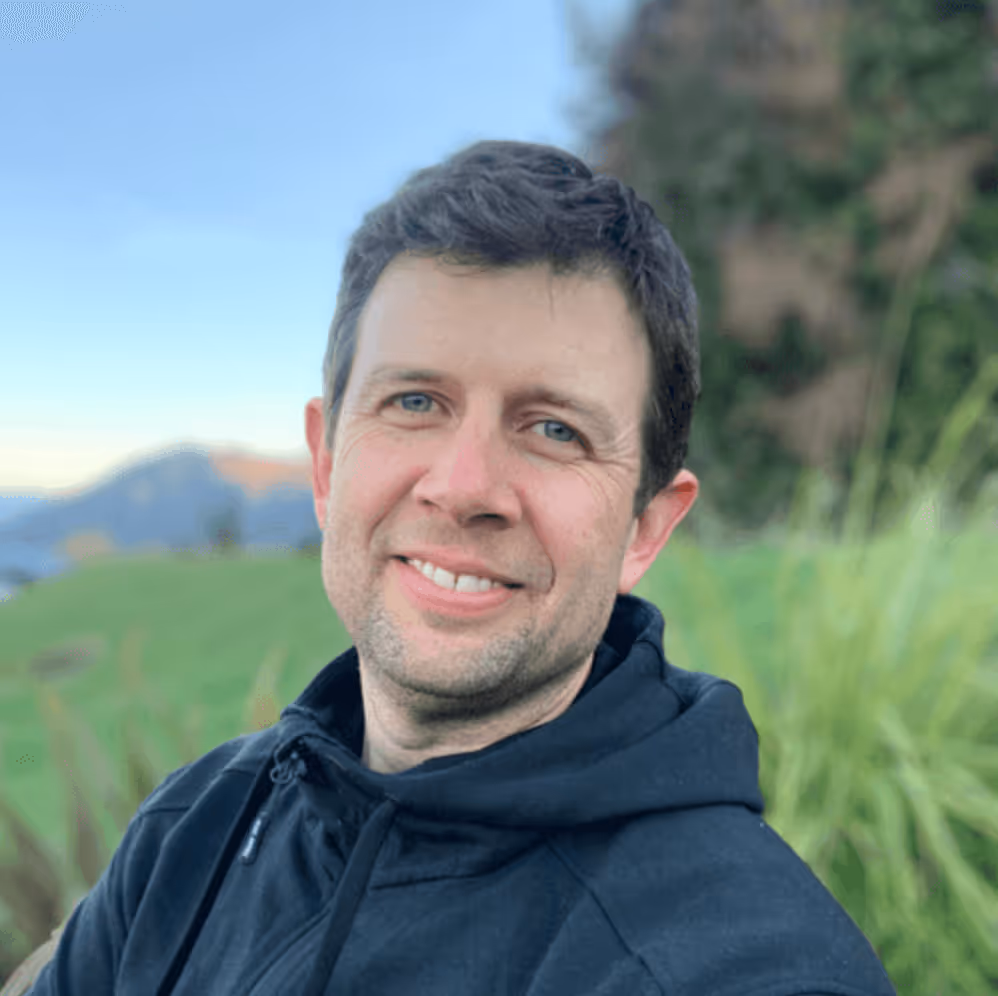 A photo of Steve smiling at the camera wearing a black hoodie against a grassy green background