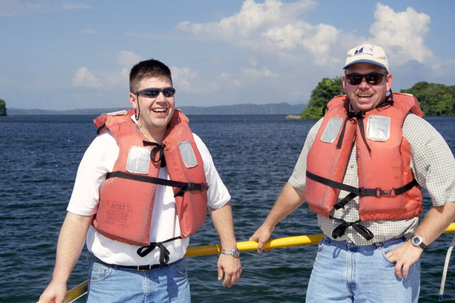Two men wearing life vests are smiling and standing on a boat.