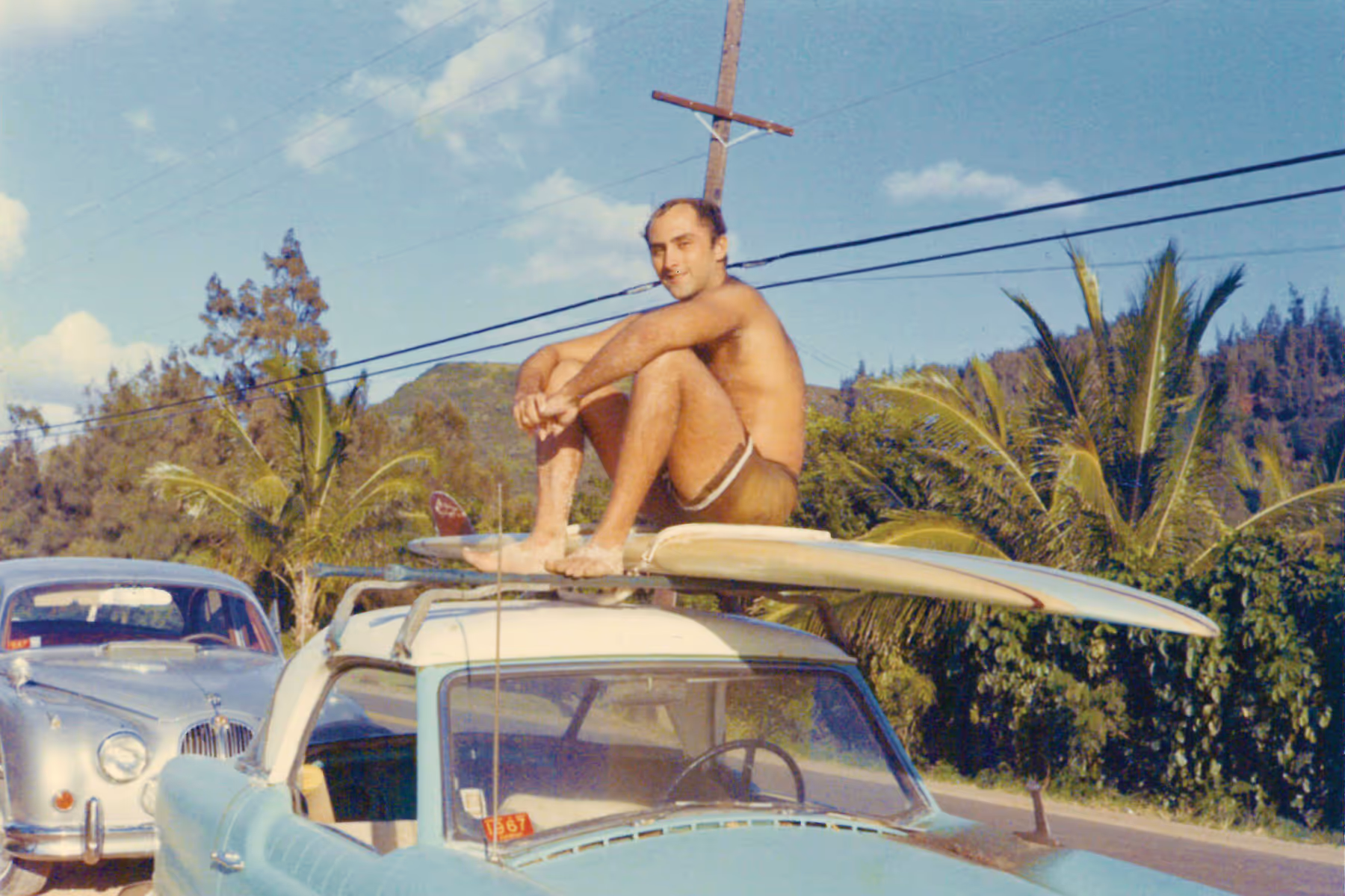 A man is sitting on a surfboard on top of a car.