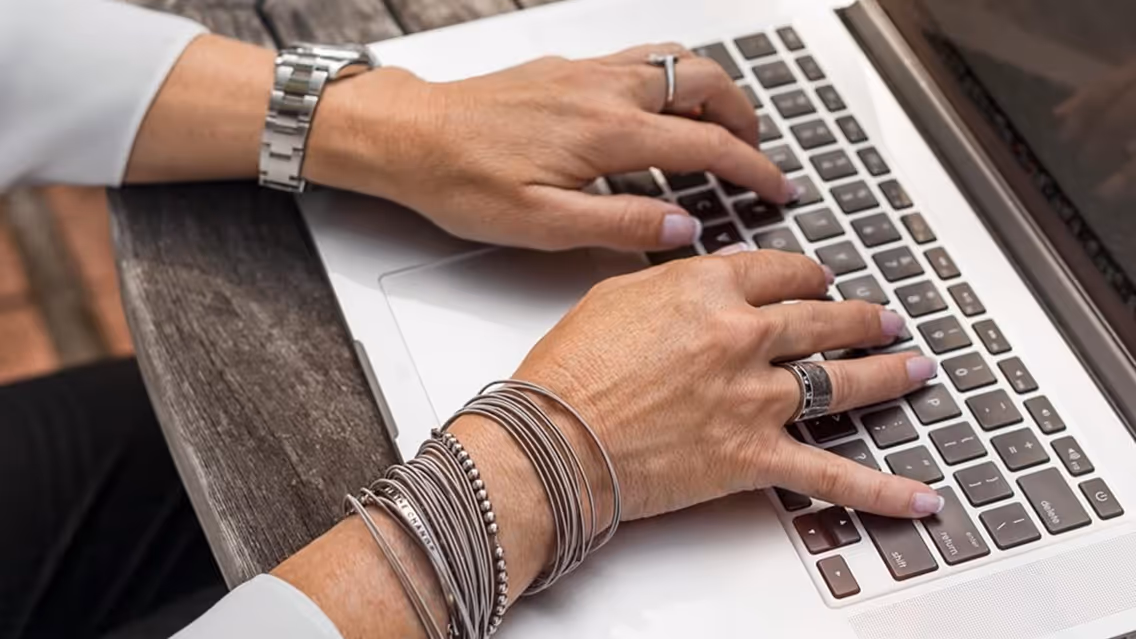A person wearing a watch and bracelets is typing on a laptop.