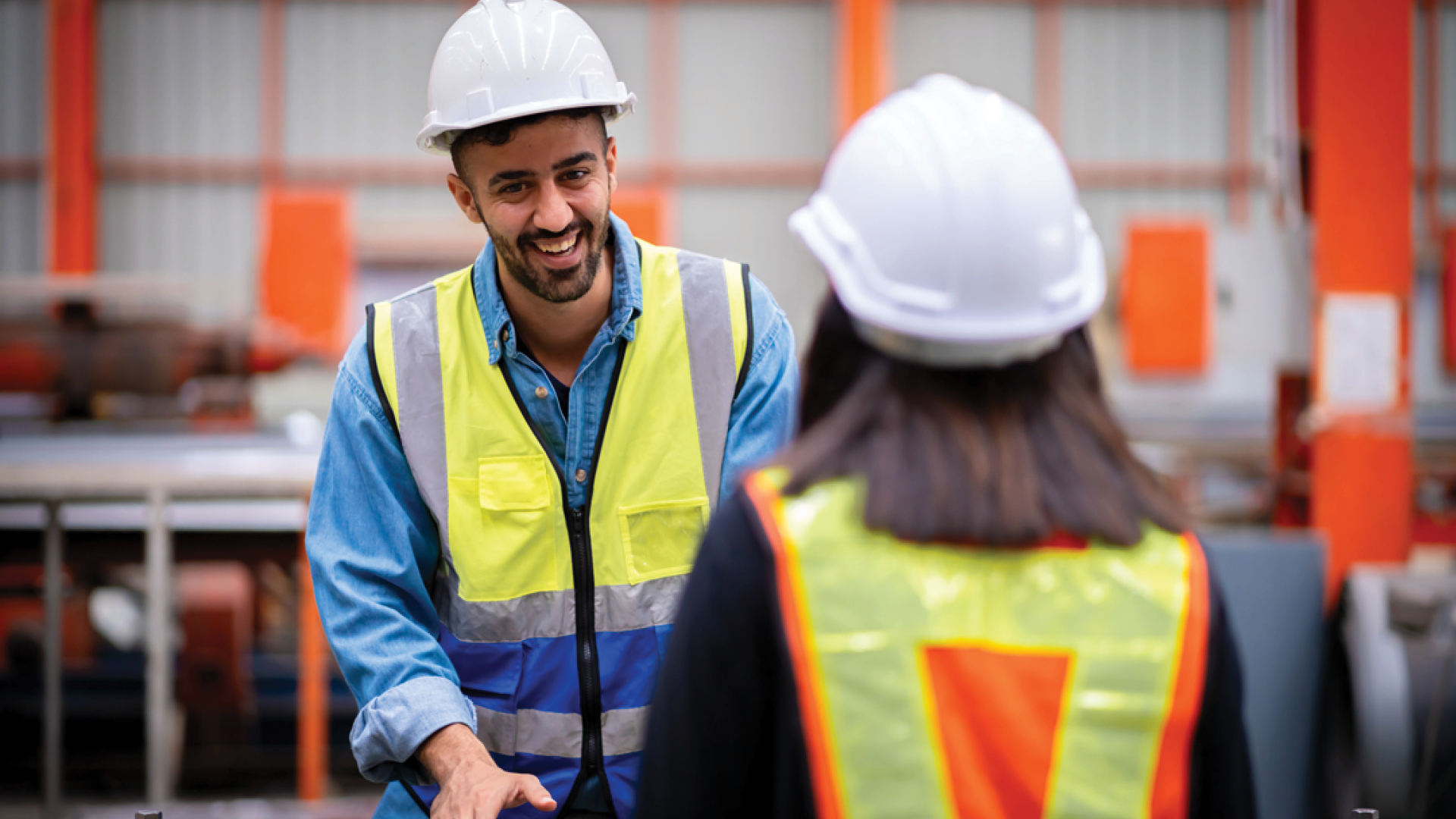 Worker in hard hat smiles at co-worker whose back is to camera. 