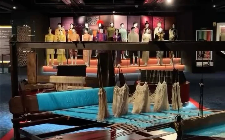 The Pameran Fabrik ASEAN textile exhibition at Muzium Negara, with a traditional loom in front of the costume displays