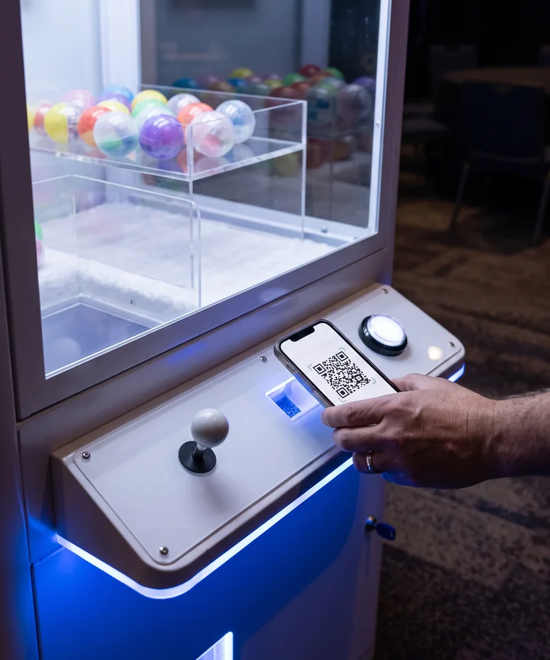 Product render of a guest holding a phone with a QR code to the scanner on the claw machine control panel