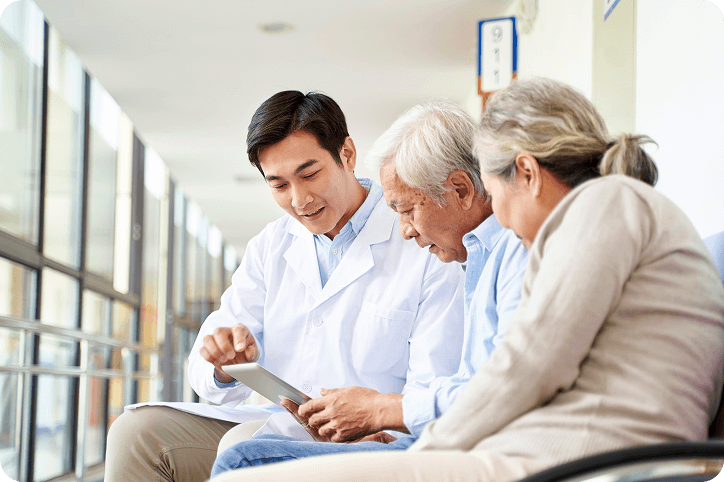 A doctor shows an older couple information on a tablet at a medical facility while discussing patient payment plans.