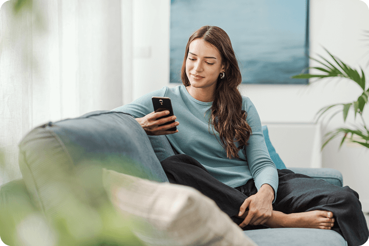 A woman sitting on a couch smiling at her phone, representing a customer comparing Affirm vs Afterpay payment options.
