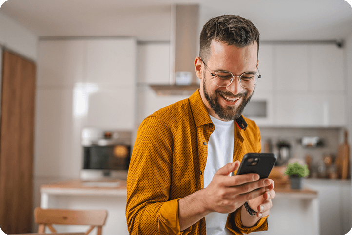 A smiling man looks at his phone in a kitchen, representing a customer comparing Affirm vs Cherry payment plans.