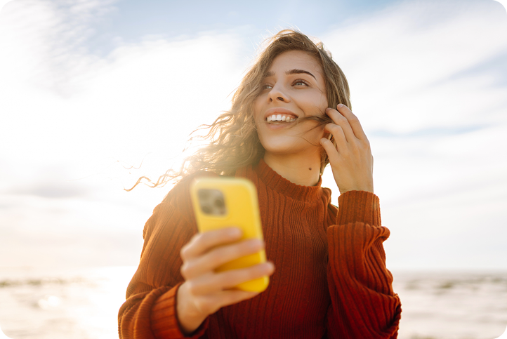 A smiling woman holding a yellow phone outdoors, representing a customer exploring Vagaro alternatives.