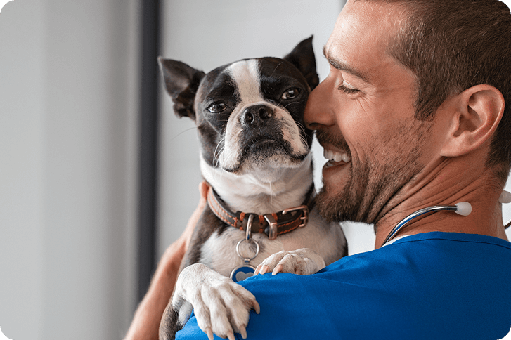 A happy pet owner holds their dog at the vet after being referred by a friend through a veterinary referral program.
