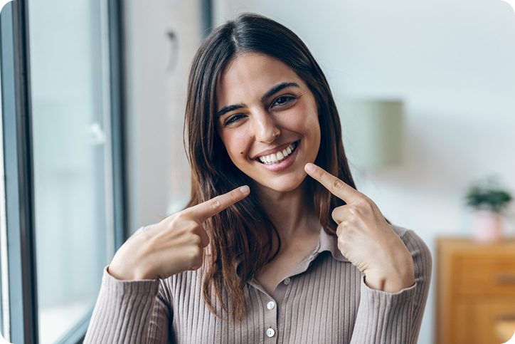 A smiling woman points to her teeth, representing patients exploring Sunbit dental financing and alternatives.