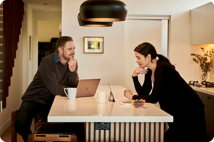 A couple sits at a kitchen island reviewing medical credit card options together on a laptop and tablet.