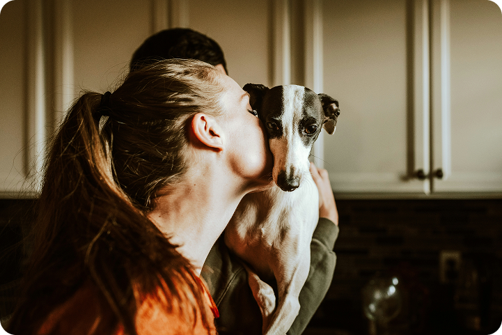 A woman kisses her dog at home, representing a pet owner exploring pet credit card options.