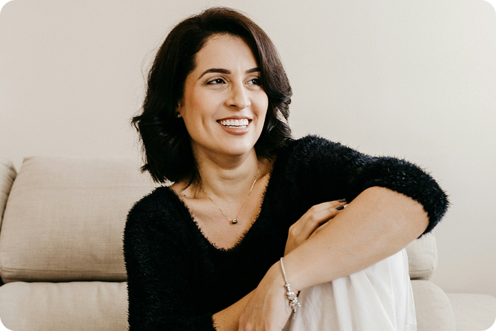 A smiling woman sits comfortably on a couch at home, representing a patient exploring plastic surgery credit card options.