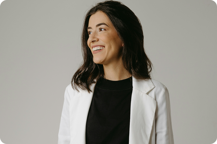 A smiling professional woman in a white blazer looks to the side, representing a customer exploring Synchrony competitors.