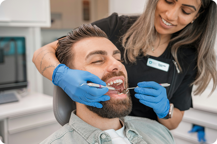 A dental hygienist performs a teeth cleaning for a patient, highlighting the use of dental practice management software in a dental office.