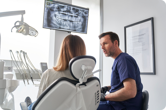 A dentist discusses treatment with a patient while reviewing a dental X-ray, representing concerns about Sunbit dental financing.