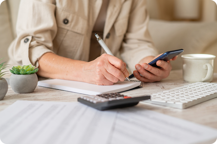 A person calculates expenses while using a smartphone, representing the risks of deferred interest financing and unexpected interest charges.