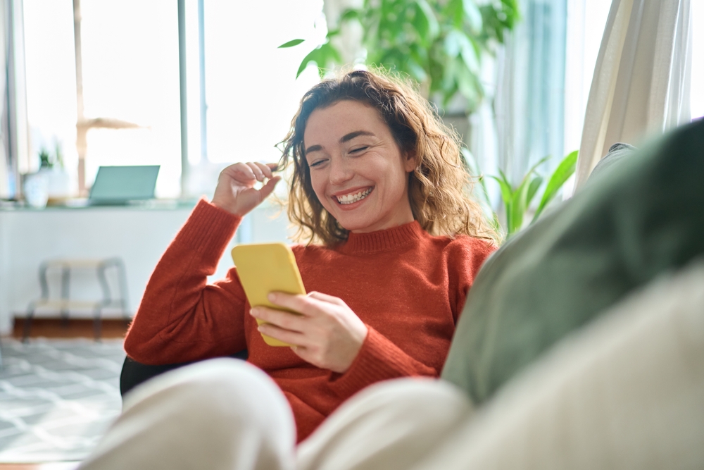 Happy woman lounging on a sofa using her phone, representing Zahara’s friendly and easy-to-use support.