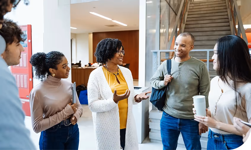 A group of people discuss an idea in a hall of what's likely a university. 