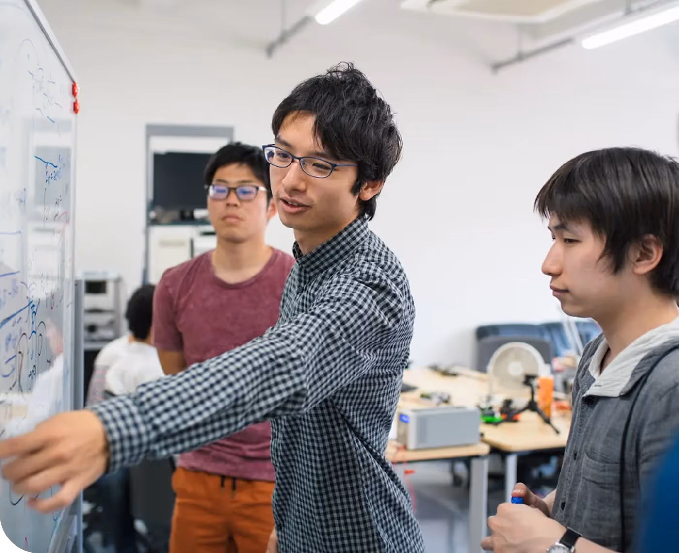 A group of men discuss an idea written on a white board, they seem to be in a class or a lab of some kind.