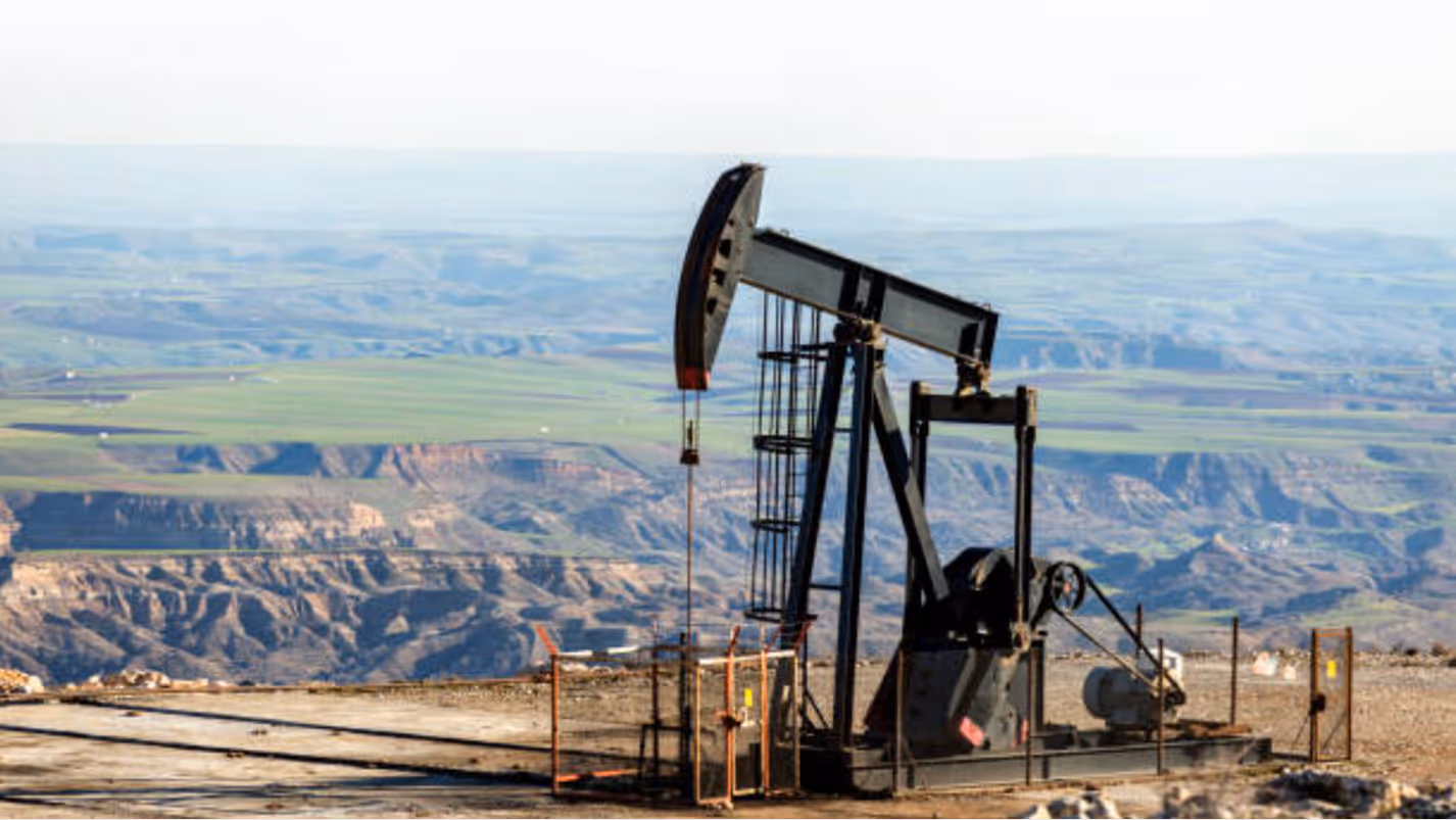 A large oil pump jack stands on a rocky, elevated plateau. 