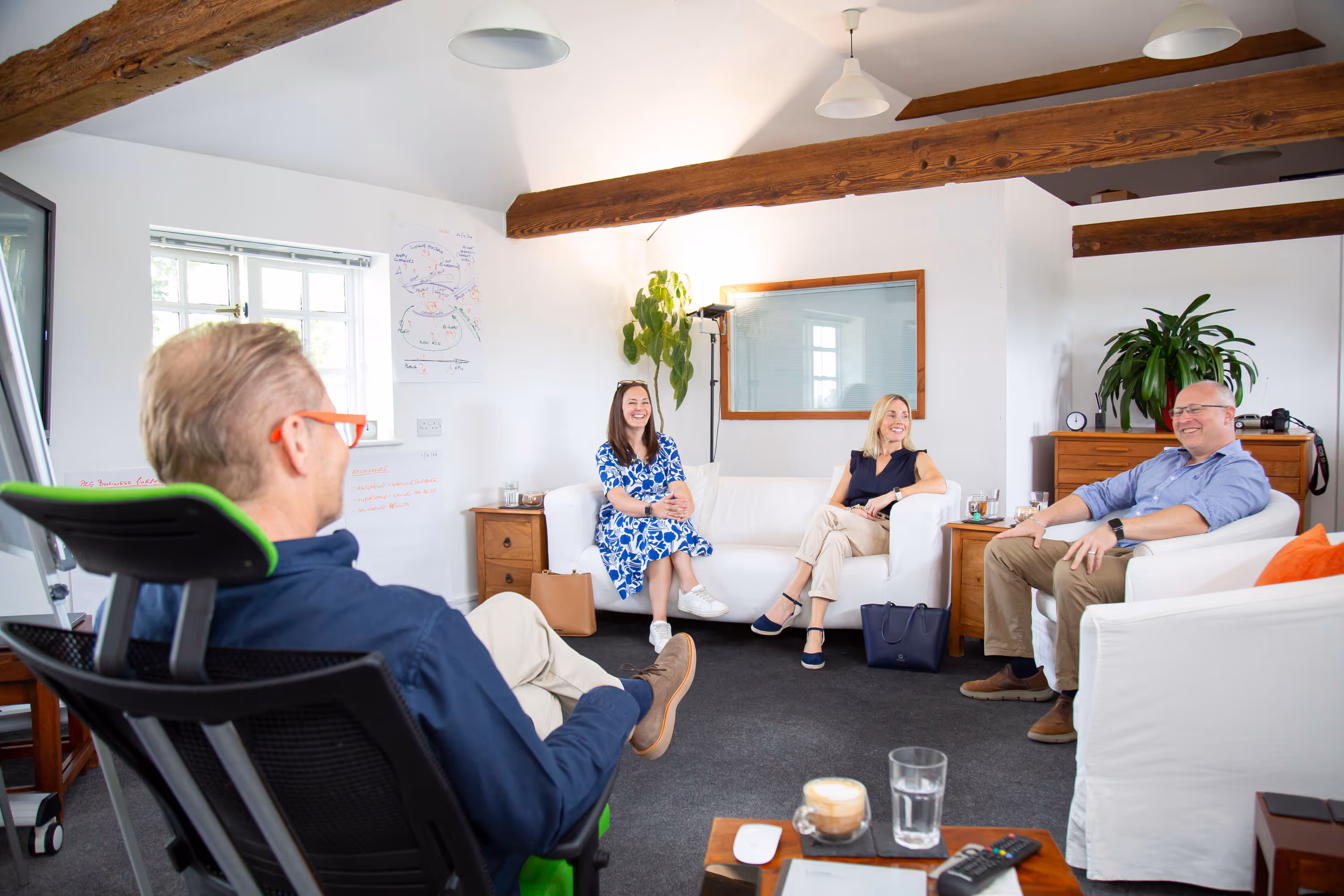 Four people sit in an office, engaged in a relaxed conversation.