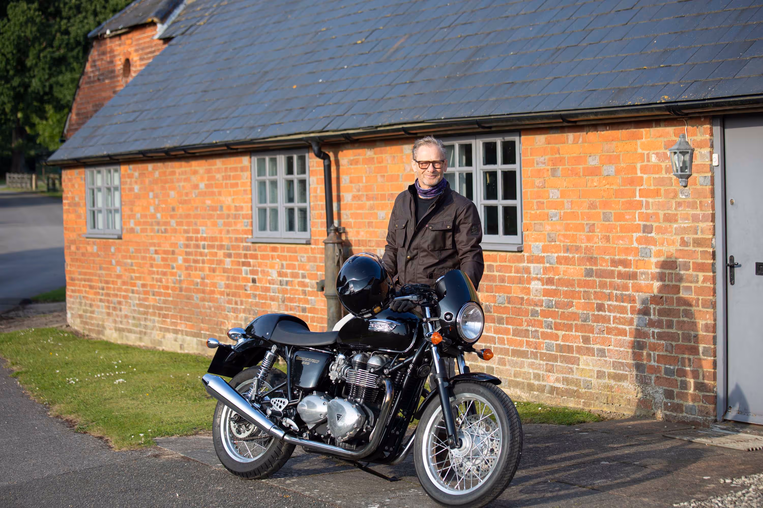 A person stands outside a brick building beside a parked black motorcycle.