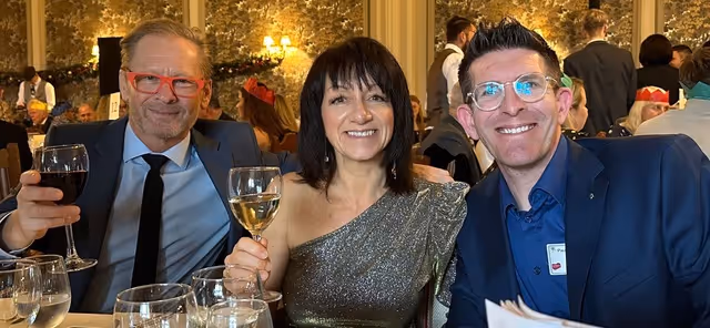 Three people smiling and holding glasses of wine at a festive gathering.