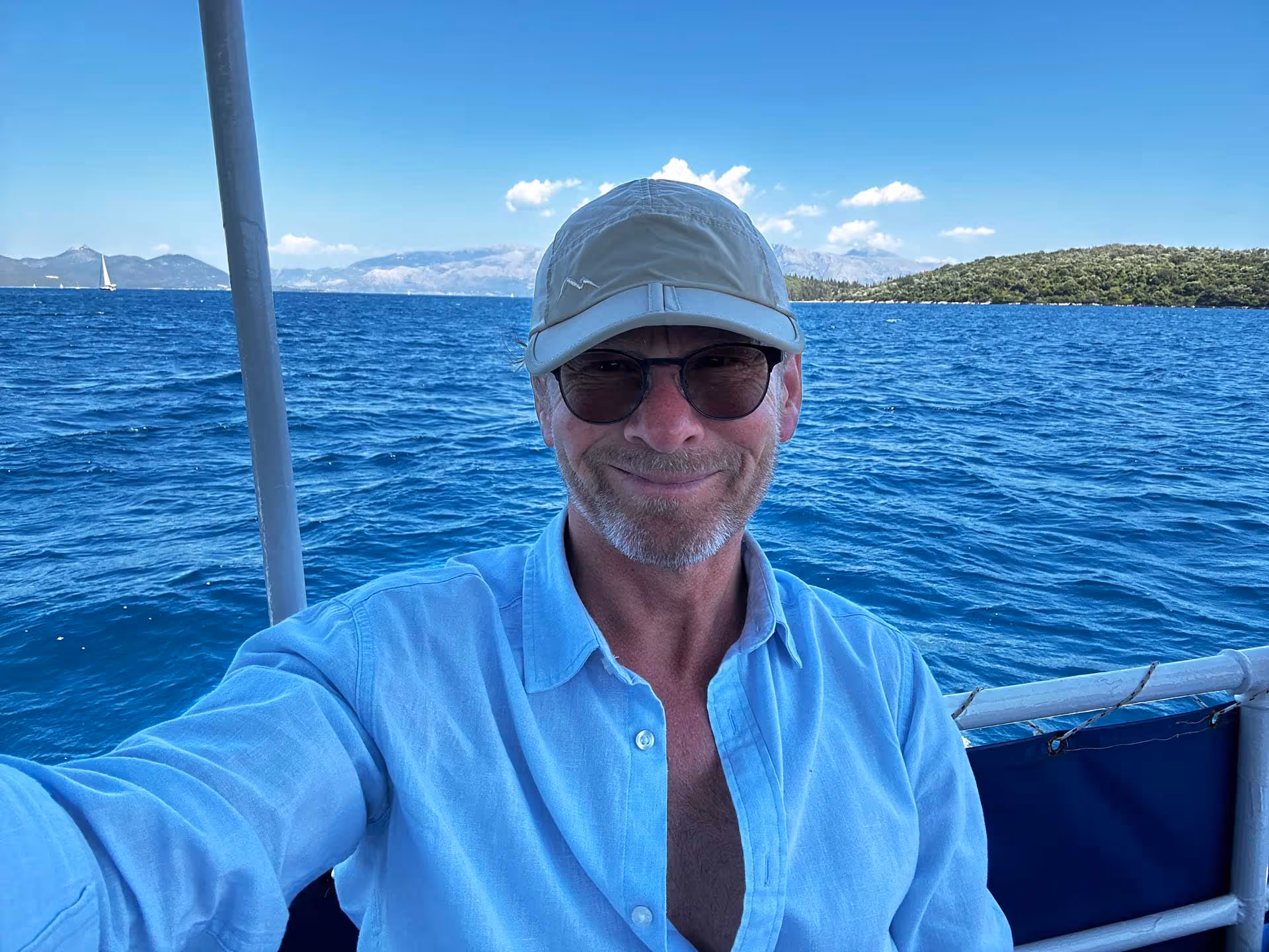 Man wearing a blue shirt and hat smiling on a boat in the ocean.