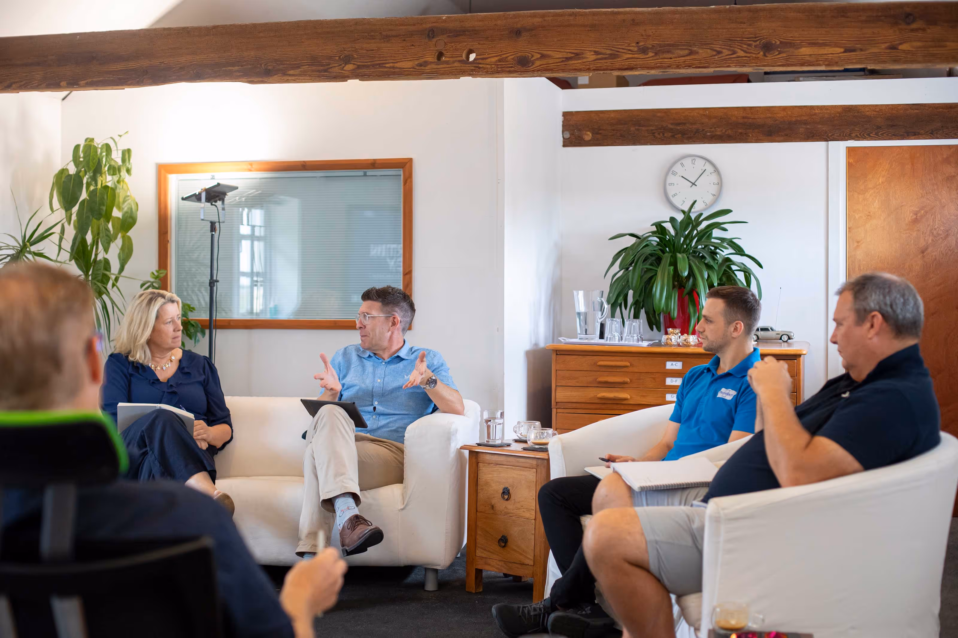 Four people sit in a meeting, having a discussion in a bright room.