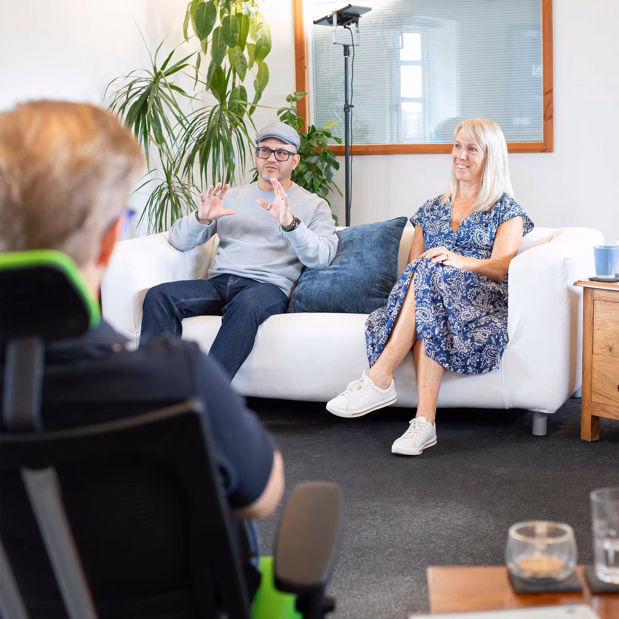 Man and woman sitting on a couch, talking to a person seated in an office chair.