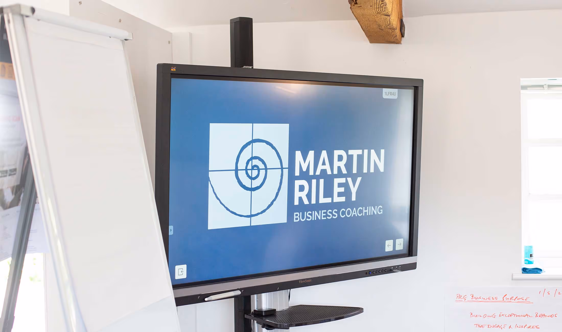 Interactive screen displaying "Martin Riley Business Coaching" next to a whiteboard in an office setting.