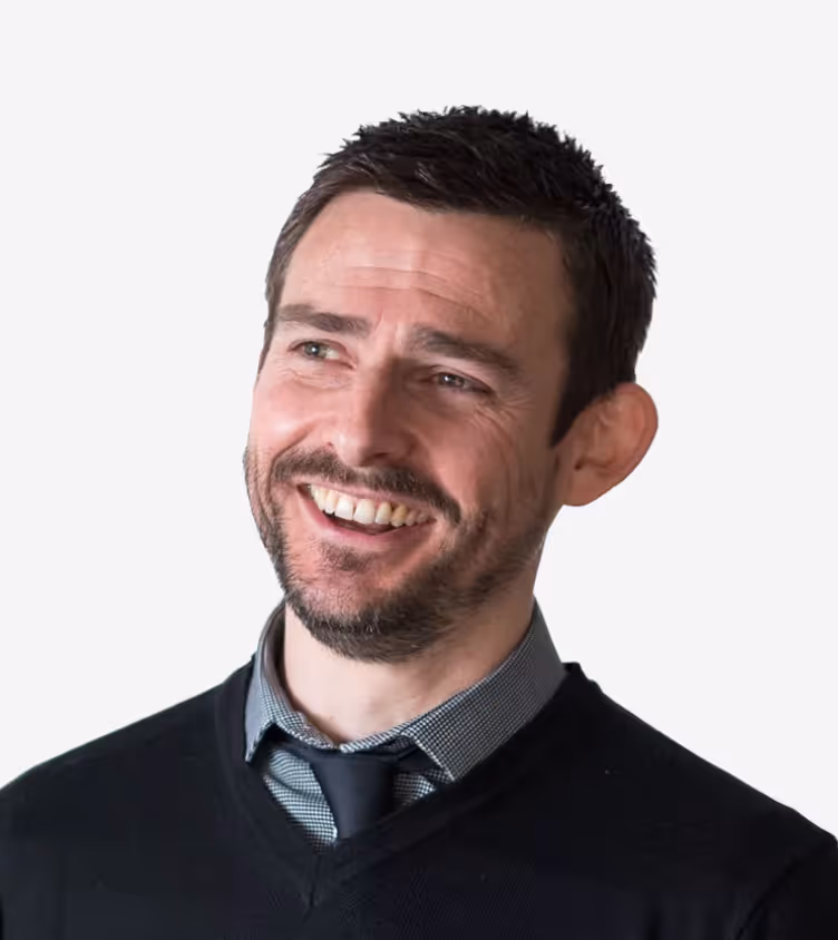 Smiling man with short hair wearing a black sweater and tie, looking to the side.