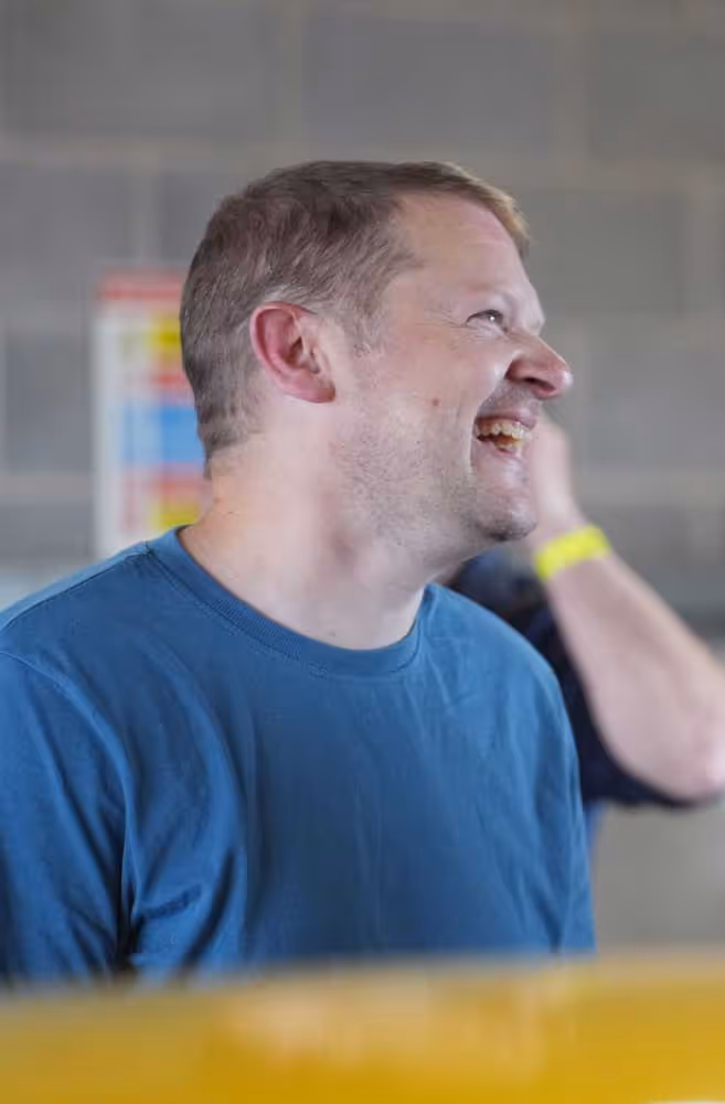 Man in a blue shirt smiling and looking to the side in an indoor setting.