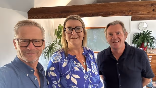 Three people smiling at the camera in an indoor setting.