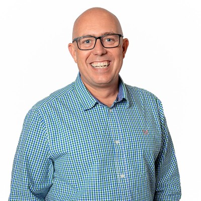 A bald man wearing glasses and a checkered shirt is smiling at the camera.