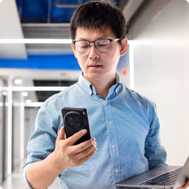 Man checking is phone while holding a laptop and walking